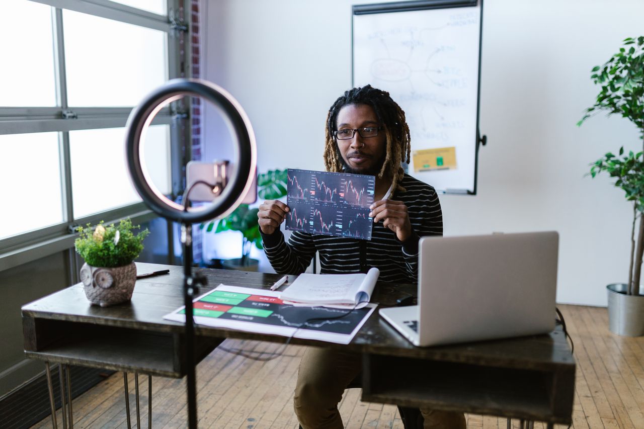our-facilities-04 A financial vlogger in a home studio discusses cryptocurrency trends using charts and a laptop.